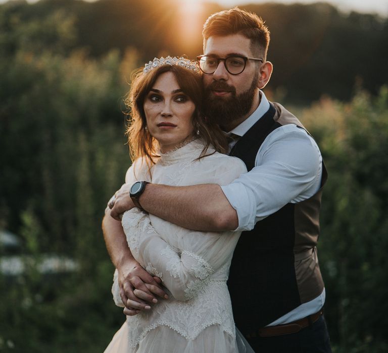 Groom wraps his arms around brides shoulders during golden hour in field 