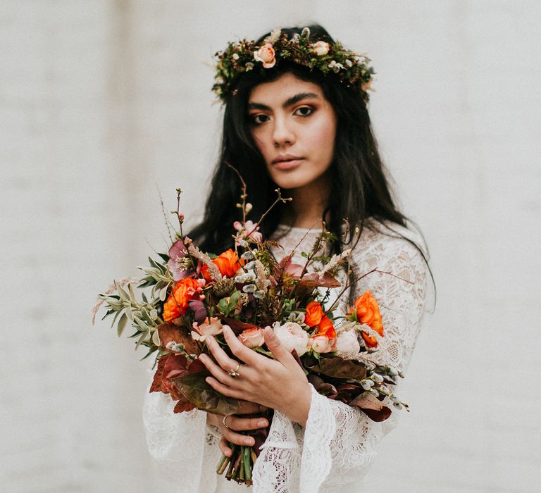 Boho bride in a lace long sleeve wedding dress holding a orange and red wedding bouquet 