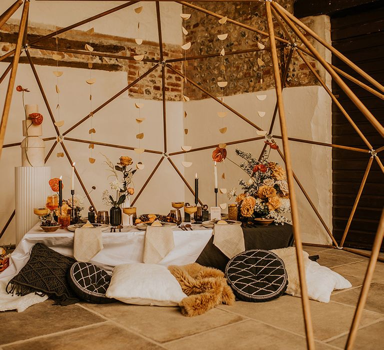 Geodome wedding reception at Curdshall Barn with black cushions, orange and yellow flowers and tall marble wedding cake 