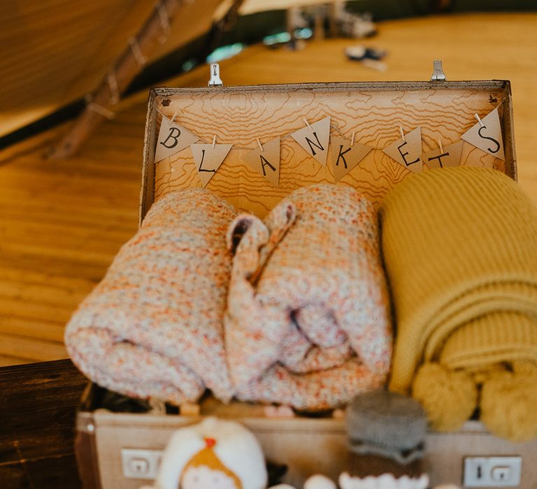 Suitcase full of blankets with bunting reading 'Blankets' inside tipi at Wellington Wood Norfolk for late summer wedding