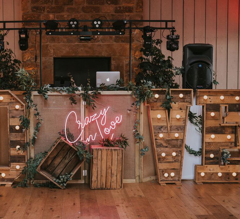 Large wooden bulb 'LOVE' sign in front of DJ booth with pink neon sign reading 'Crazy in Love' for summer wedding at Primrose Hill Farm