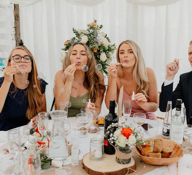 Wedding guests blow bubbles across table during reception in marquee