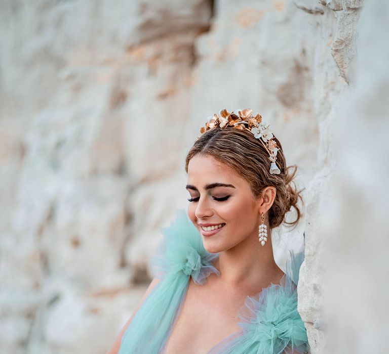 Groom with a pinned up do wearing a gold headband and dangly earrings wearing a Millia London green tulle wedding dress 