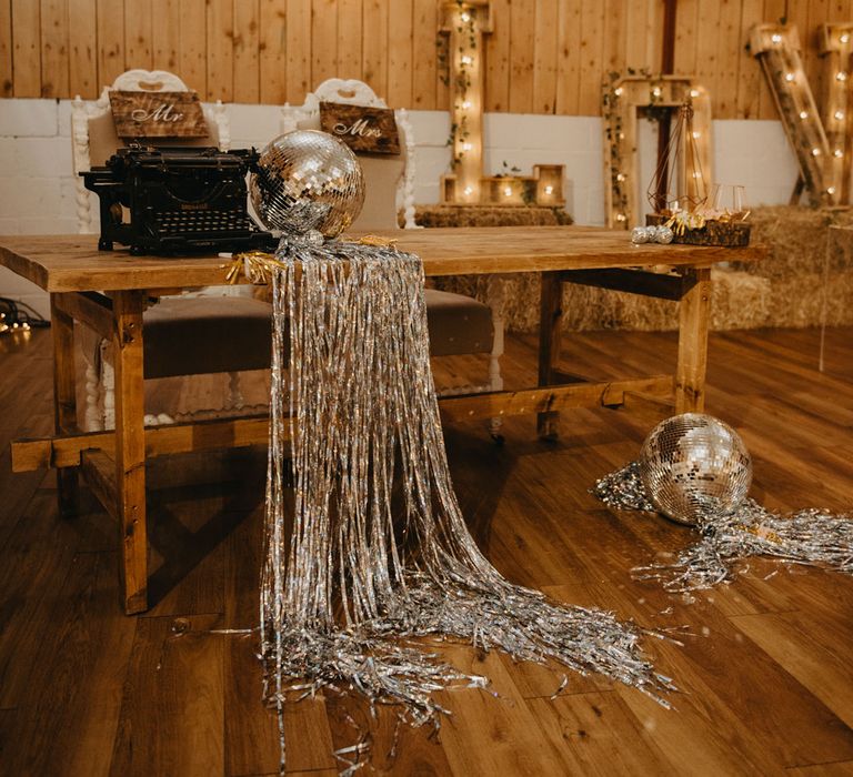 Wooden table with large wooden letters, fairy lights, disco ball and streamers for rustic wedding reception