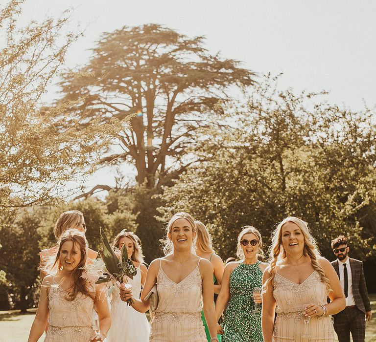 Bridesmaids wearing neutral sparkly dresses walk with one another 