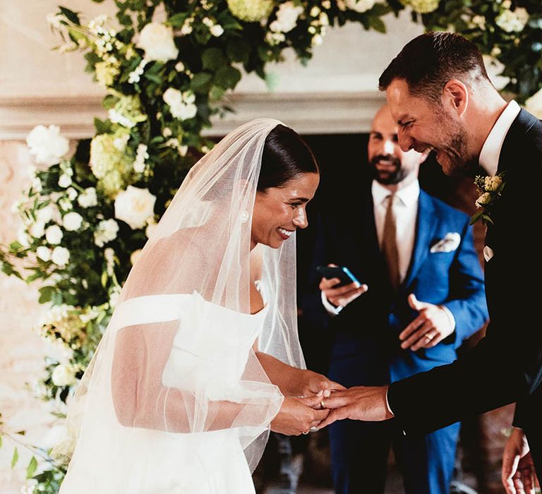 Bride & groom hold hands on their wedding day in front of florals