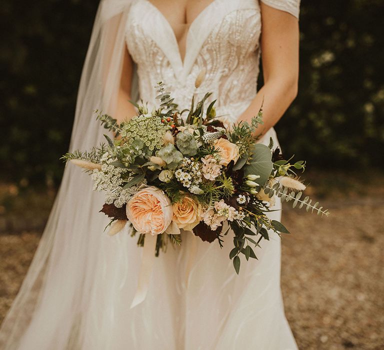 Bride clutches peach bouquet in off the shoulder wedding dress