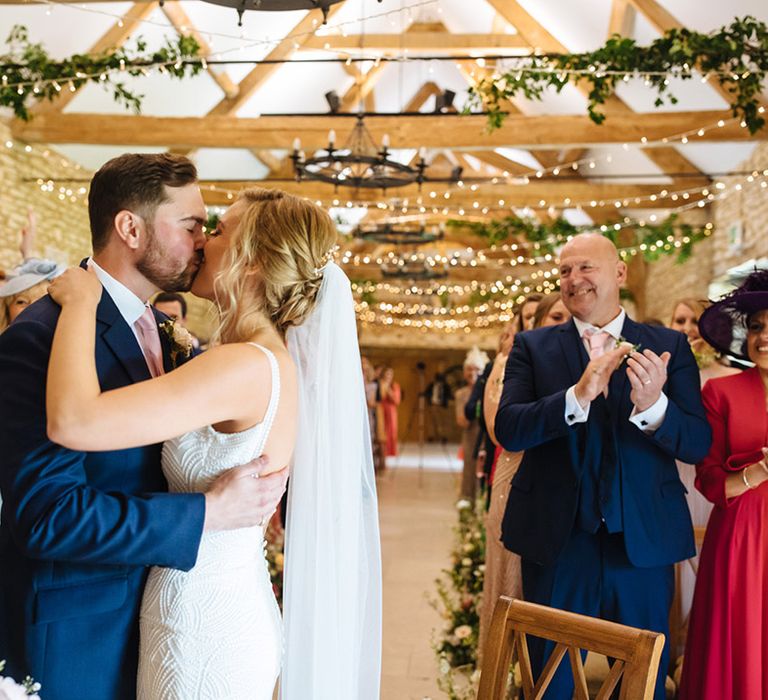 Groom in a navy suit kissing his bride at the altar in a beaded Made With Love wedding dress