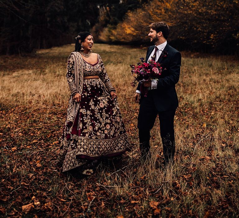 Bride wears Indian Saree wedding dress and matches in groom in dark suit holding stunning a mixture of dark & hot pink flower bouquet 