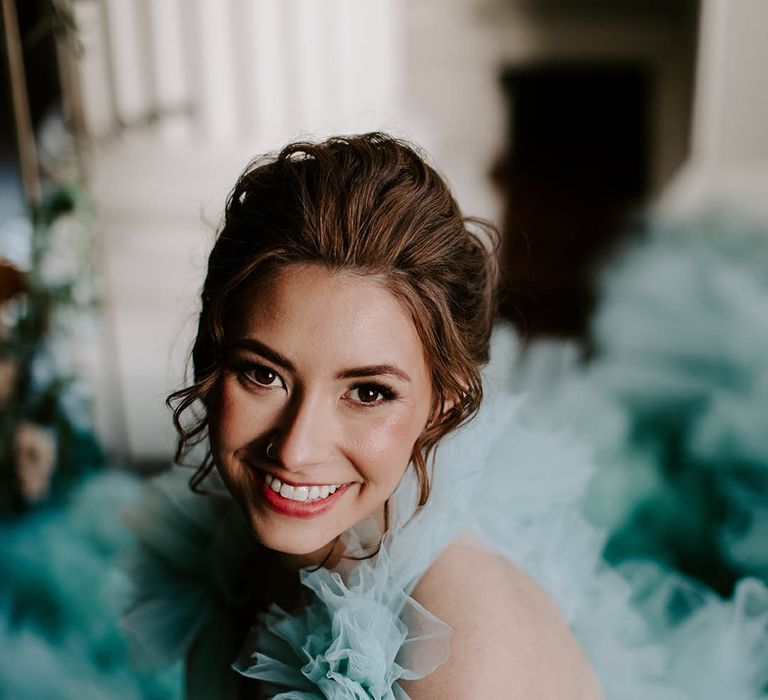 beautiful bride with a pinned bridal up do with loose tendrils, and subtle wedding makeup with a light red lipstick 