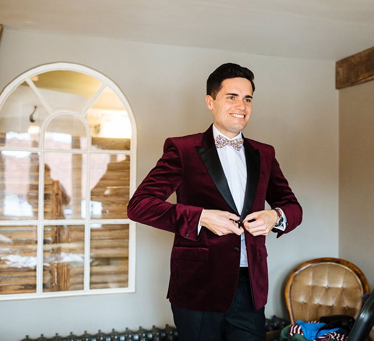 Groom gets ready for his wedding day as he does up his burgundy velvet tuxedo jacket