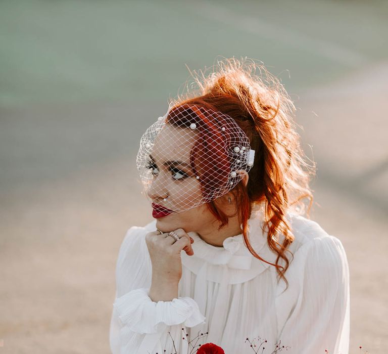 Bride in a short wedding dress and birdcage veil holding a red and pink wedding boquet with sweet peas and butterfly ranunculus 