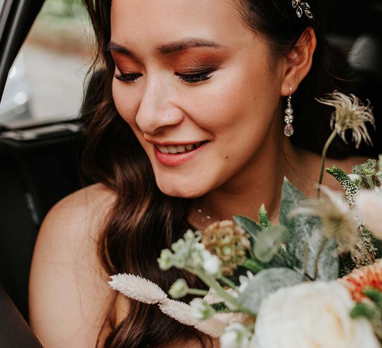 Bride with smoky eye makeup look with curled hair with pearl hair accessory holding autumnal wedding bouquet