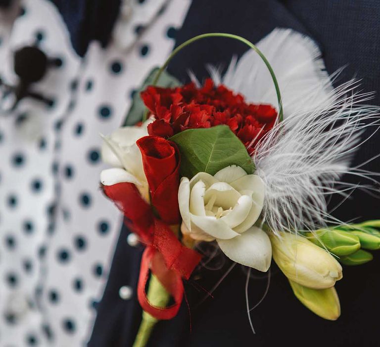 White and red floral buttonhole complete with feather