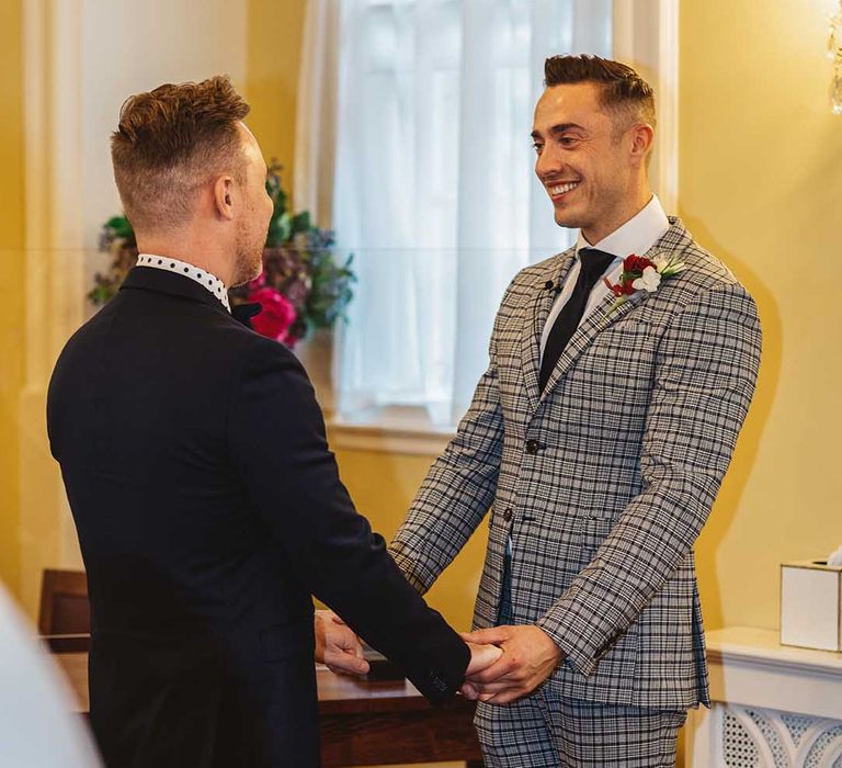 Grooms hold hands during wedding ceremony