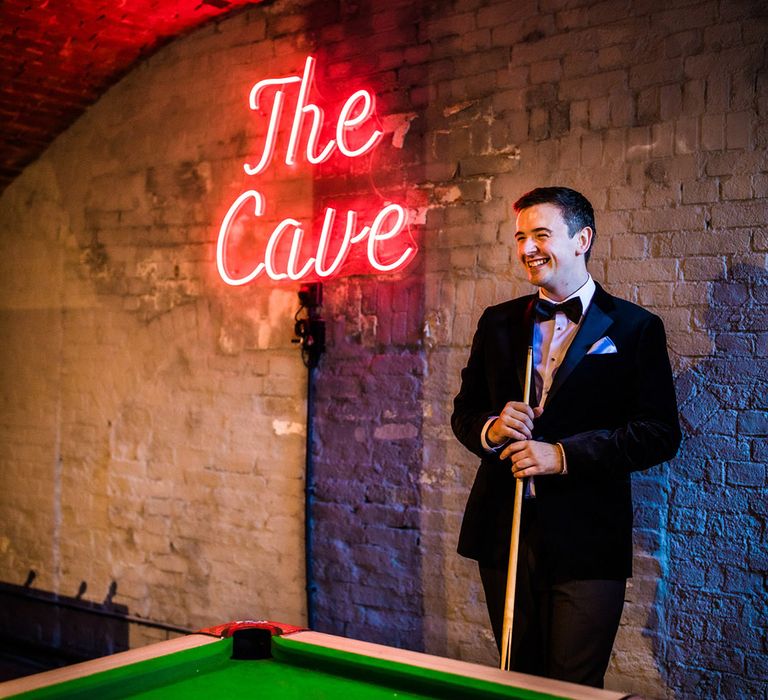 Smiling groom in black tie playing games in 'The Cave' with red neon sign