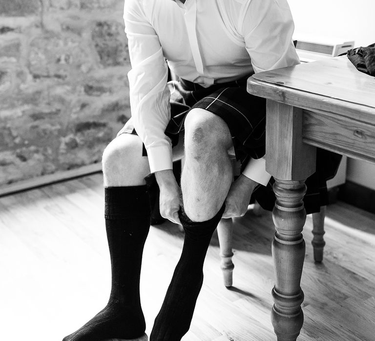 Groom gets ready for his wedding day as he puts his socks on for the big day 