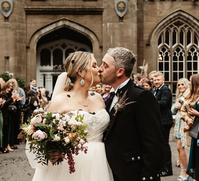 Bride and groom share a kiss outside Drumtochty Castle wedding venue with black circle confetti