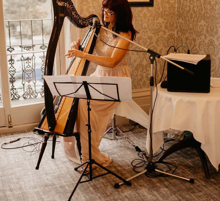 Harpist playing the harp with golden-tinted background in white embellished dress