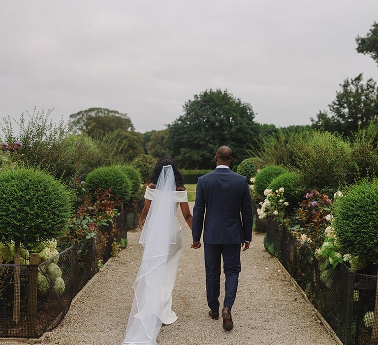 Bride and groom walk hand in hand around the gardens of Middleton Lodge wedding venue