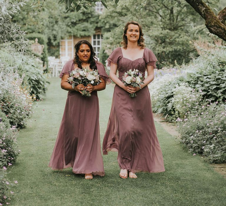 Bridesmaids in vintage pink/purple dresses holding purple flower bouquets together