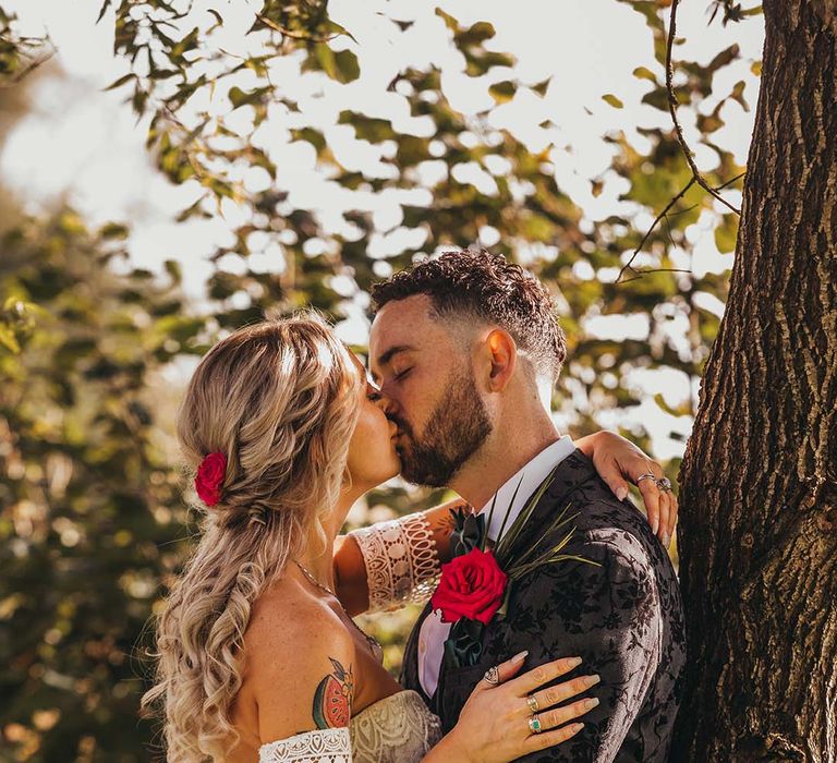 Bride and groom share a loving kiss against a tree after their outdoor wedding ceremony