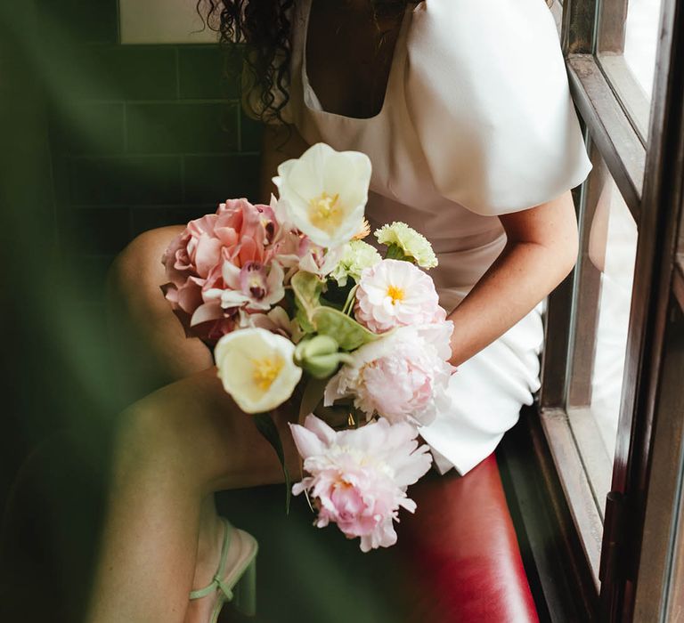 Bride in a short wedding dress with naturally curly hair holding a pink and green wedding bouquet 