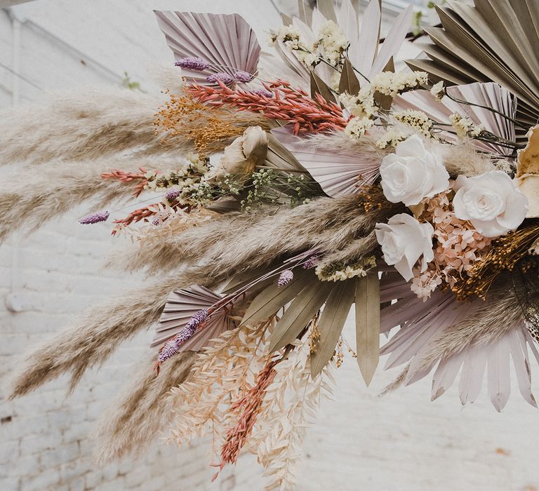 Wedding reception table decor with a pink table cloth, pillar candles mixed with cream candlesticks and preserved pastel flowers and dried grasses 