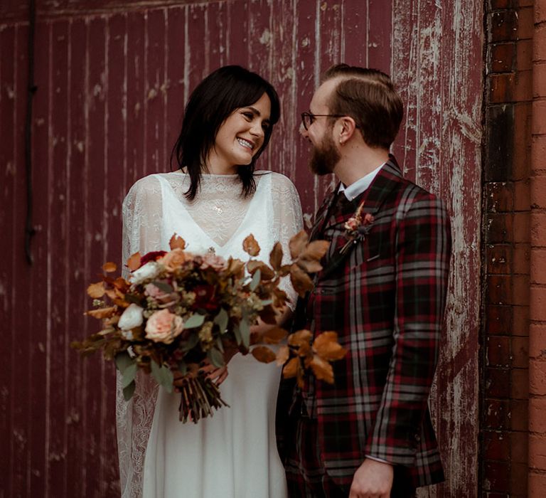 Groom wears bespoke tartan suit on his wedding day and bride wears lace cape and holds Autumnal inspired bouquet 