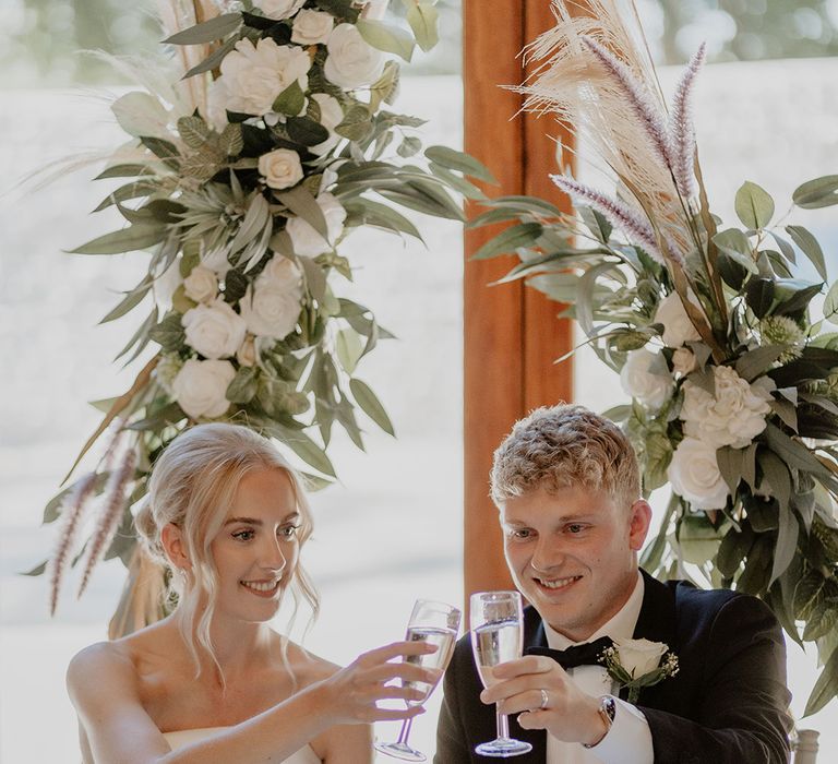 Bride and groom cheers each other as they sit for their wedding reception 