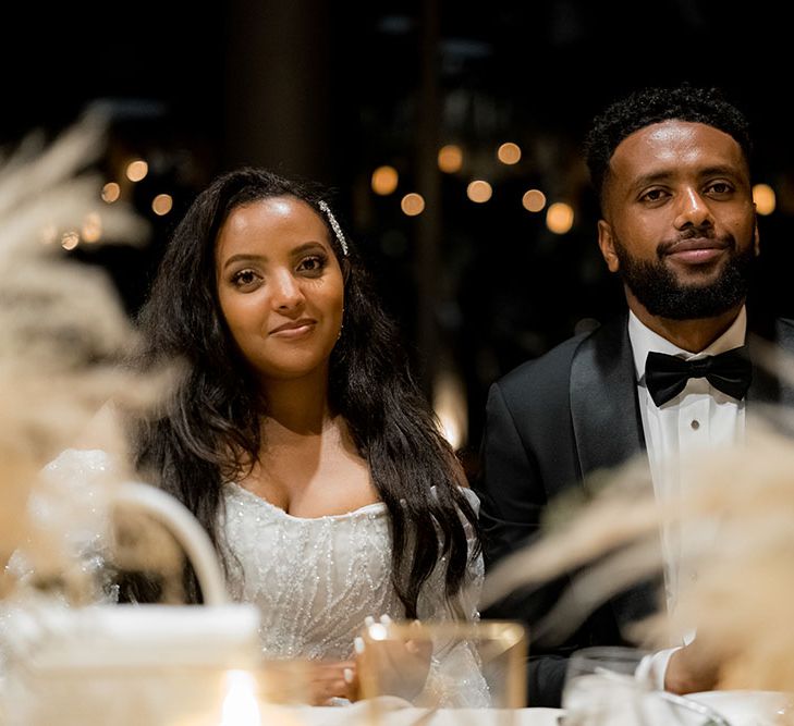 Bride wears long sleeved off-the-shoulder sparkly reception dress during wedding reception 