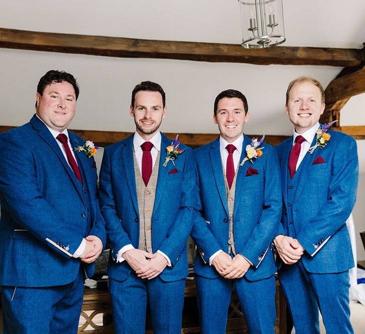 Groom and his groomsmen wear three piece suits with blue jackets, tartan waistcoats and bright floral buttonholes 