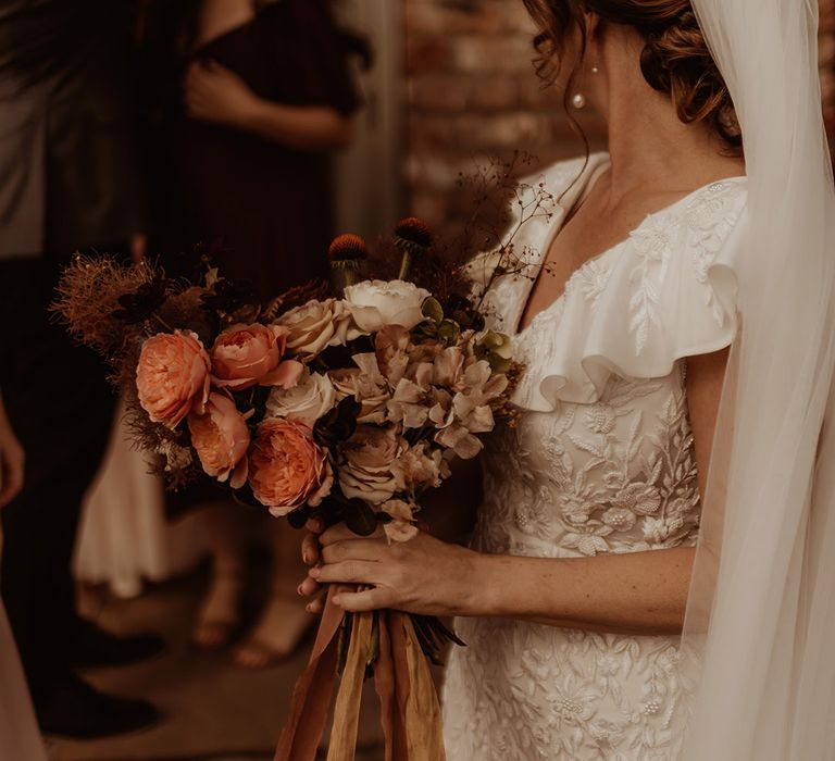 Soft muted pinks and cream wedding bouquet with the bride wearing an embroidered and beaded Emma Beaumont Atelier wedding dress