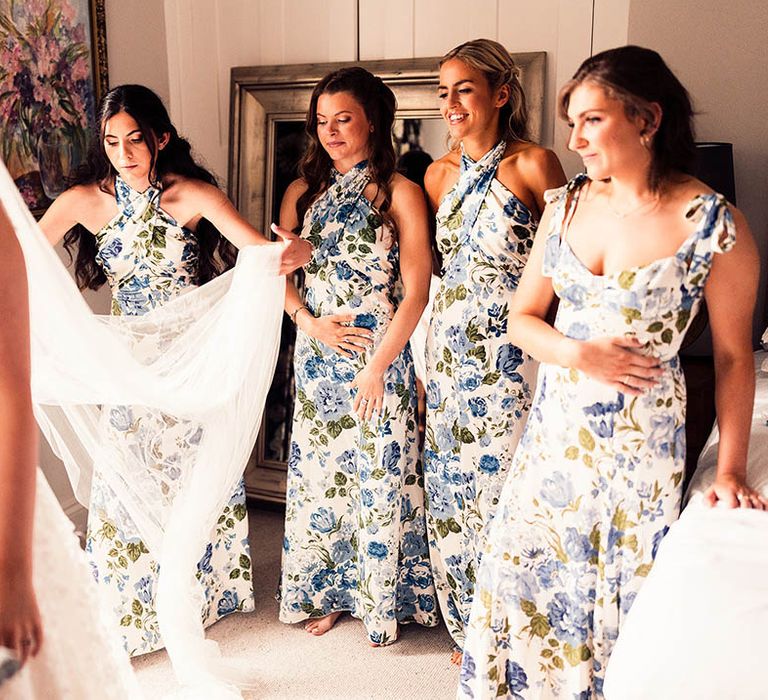 Bridesmaids in white and blue floral dresses help the bride with finishing touches as she gets ready for her wedding 