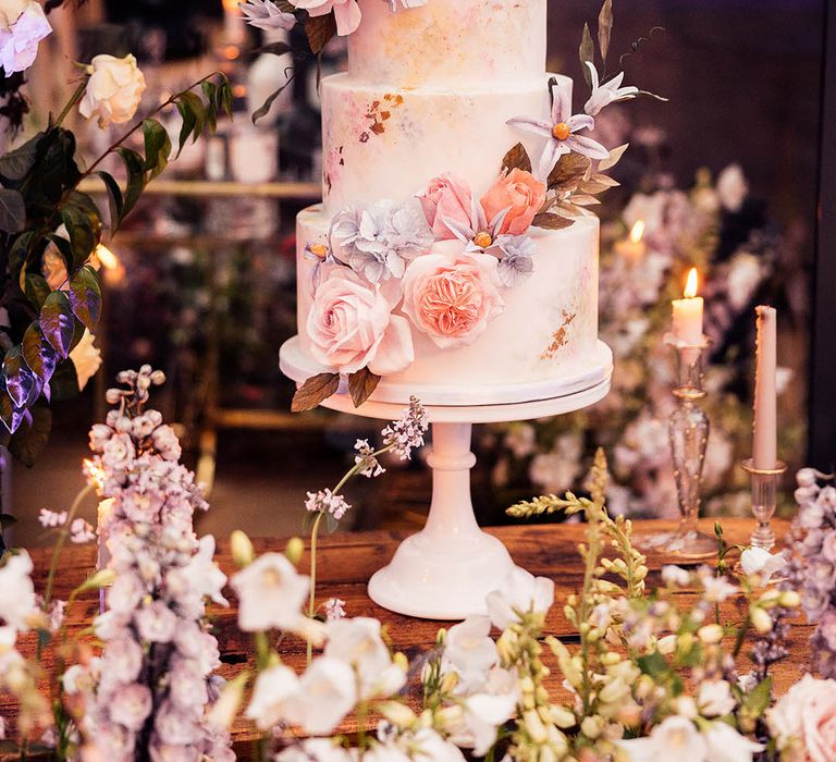 Four tier pastel water colour effect wedding cake with pink and purple pastel flowers with gold flakes