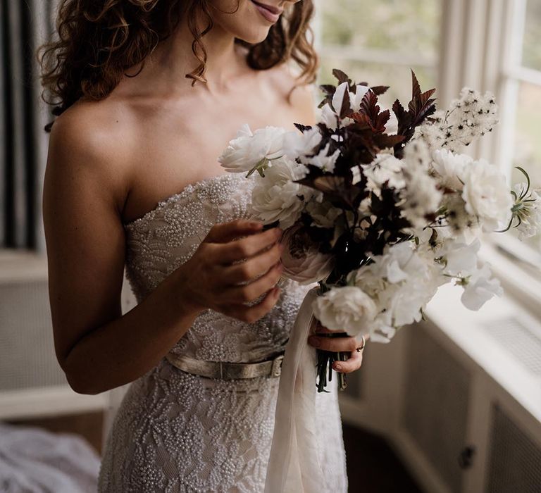 Bride in sleeveless lace wedding dress with pearl details, pearl headband and black and white minimal floral bouquet