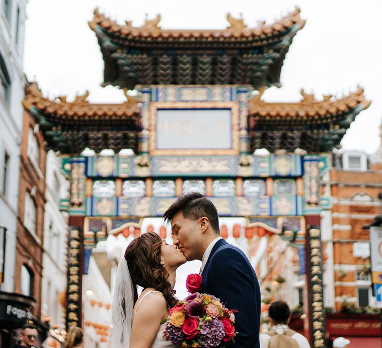 Bride & groom look lovingly at one another in China Town in London on their wedding day after taking London bus