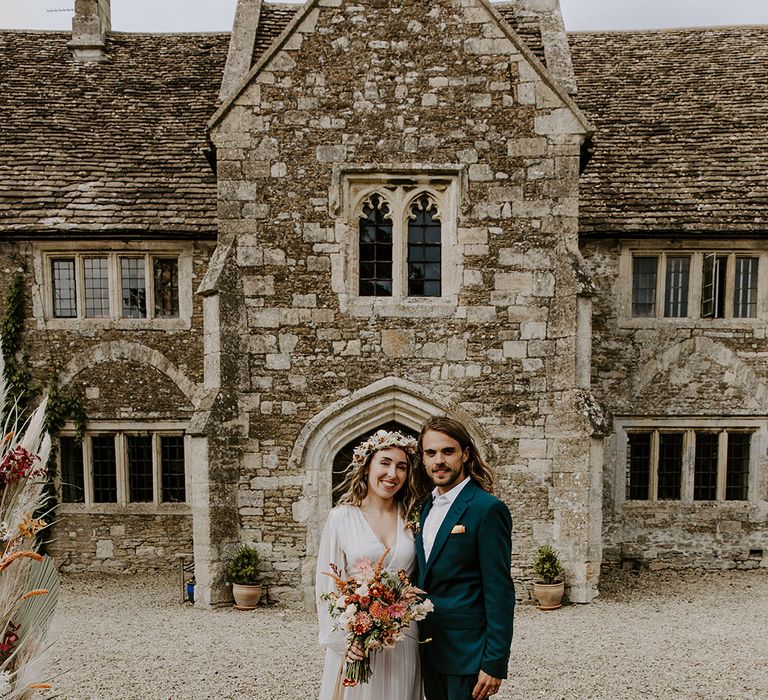 Bride holds colourful floral bouquet and stands with her groom in front of Moroccan styled rug outdoors