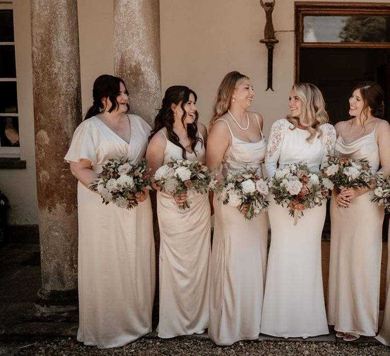 Bridesmaids in satin champagne gold dresses smiling with the bride in a long sleeve wedding dress 