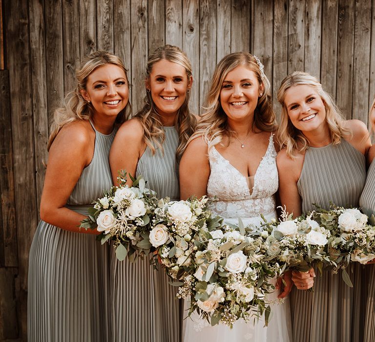 Bride in a lace Christina K wedding dress with the bridesmaids in halter neck sage green pleated bridesmaid dress