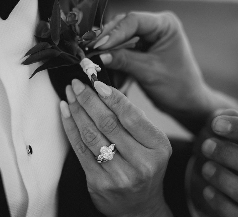 Bride helps pin her grooms floral buttonhole in black & white image