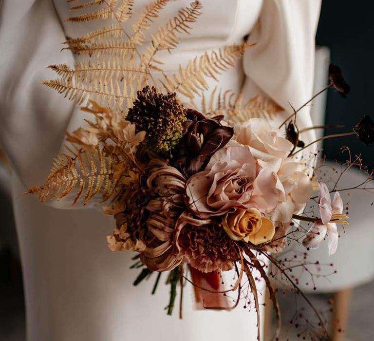 Bride holding neutral wedding bouquet with dark red, pink, orange flowers and dried grass 