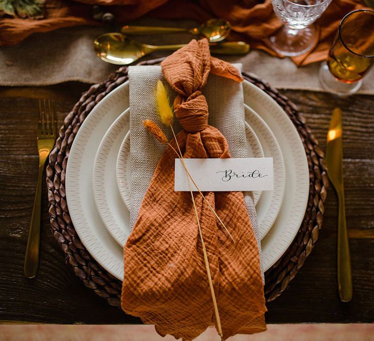 Hemp stitched linen burnt orange napkin with two pieces of autumnal coloured dried florals on autumnal boho wedding tablescape