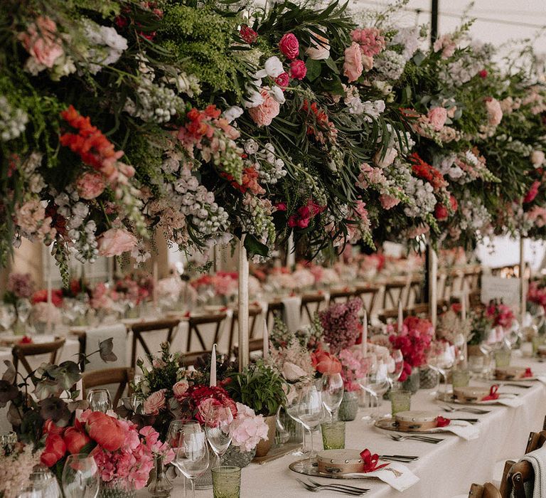 All pink wedding flower arrangements decorating the wedding reception with flower installations and table decorations with tambourine favours and coloured glassware 