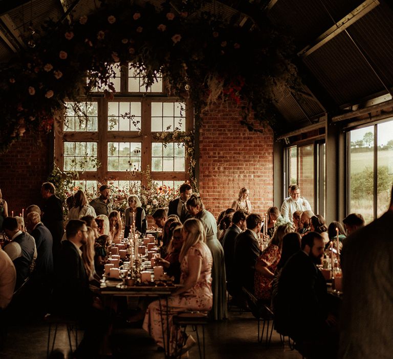 Wedding guests having their dinner in the reception room at The Giraffe Shed with large rose and foliage hanging floral decoration