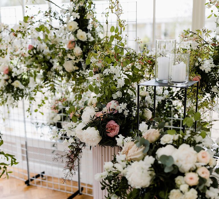 White & pink floral arrangements in modern styled vases beside white pillar candles 