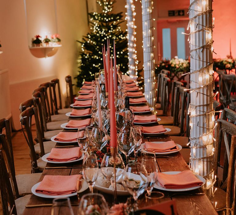 Neutral Christmas inspired tablescape with orange napkins, orange tapered candles, gold candlestick holders, a large Christmas tree and fairy lights 