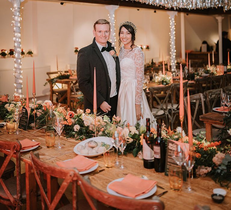 Bride and groom standing in reception room of Marylebone Town Hall with silver and gold wedding streamers, orange tapered candles, orange napkins, orange rose and foliage tablerunners and fairy lights 