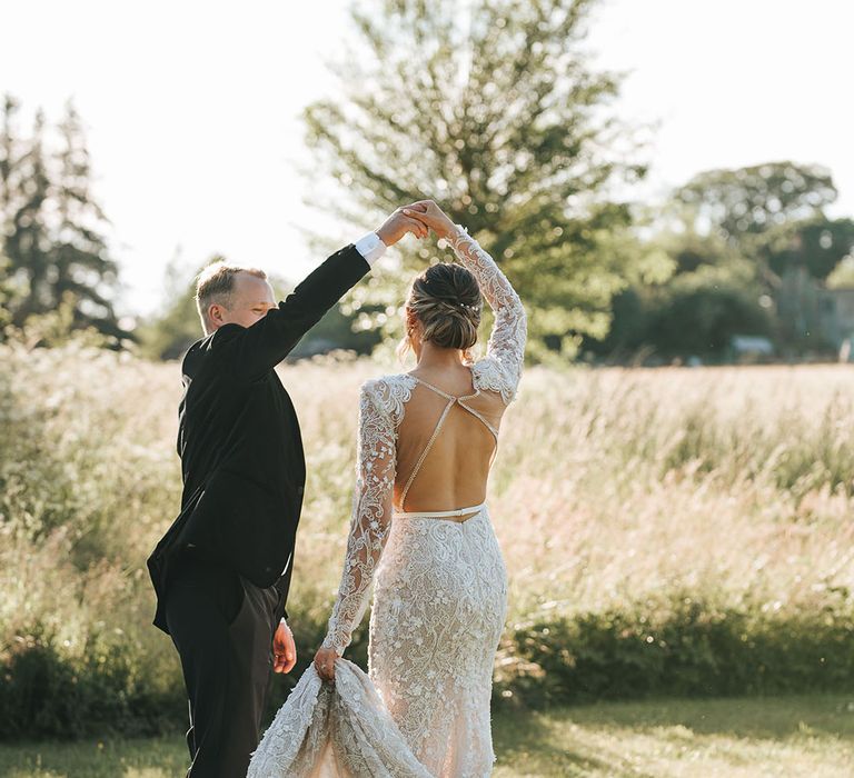 Bride in white low block heel shoes in floral lace wedding dress with open back being spun around by the groom in black tie 