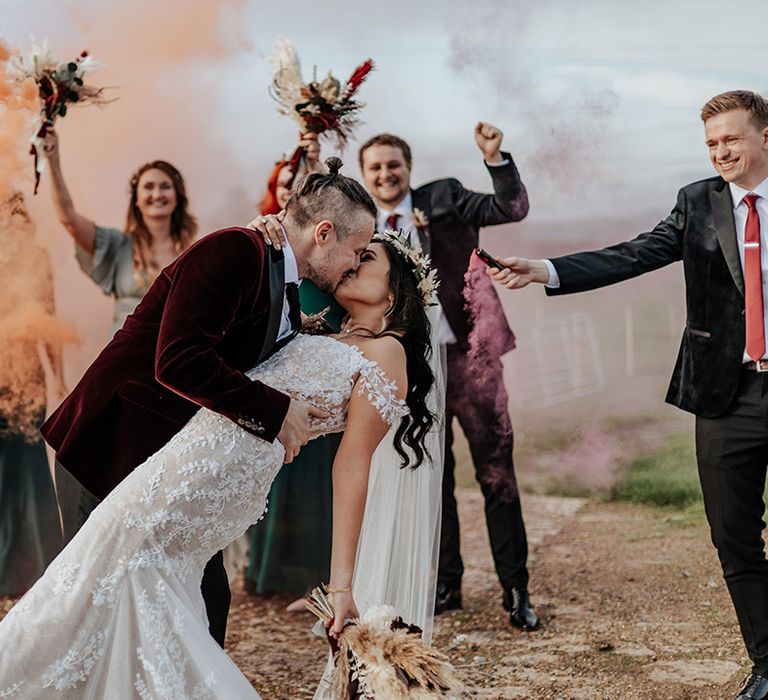 Smoke bomb wedding photoshoot with the groom tipping the bride back and giving her a kiss 